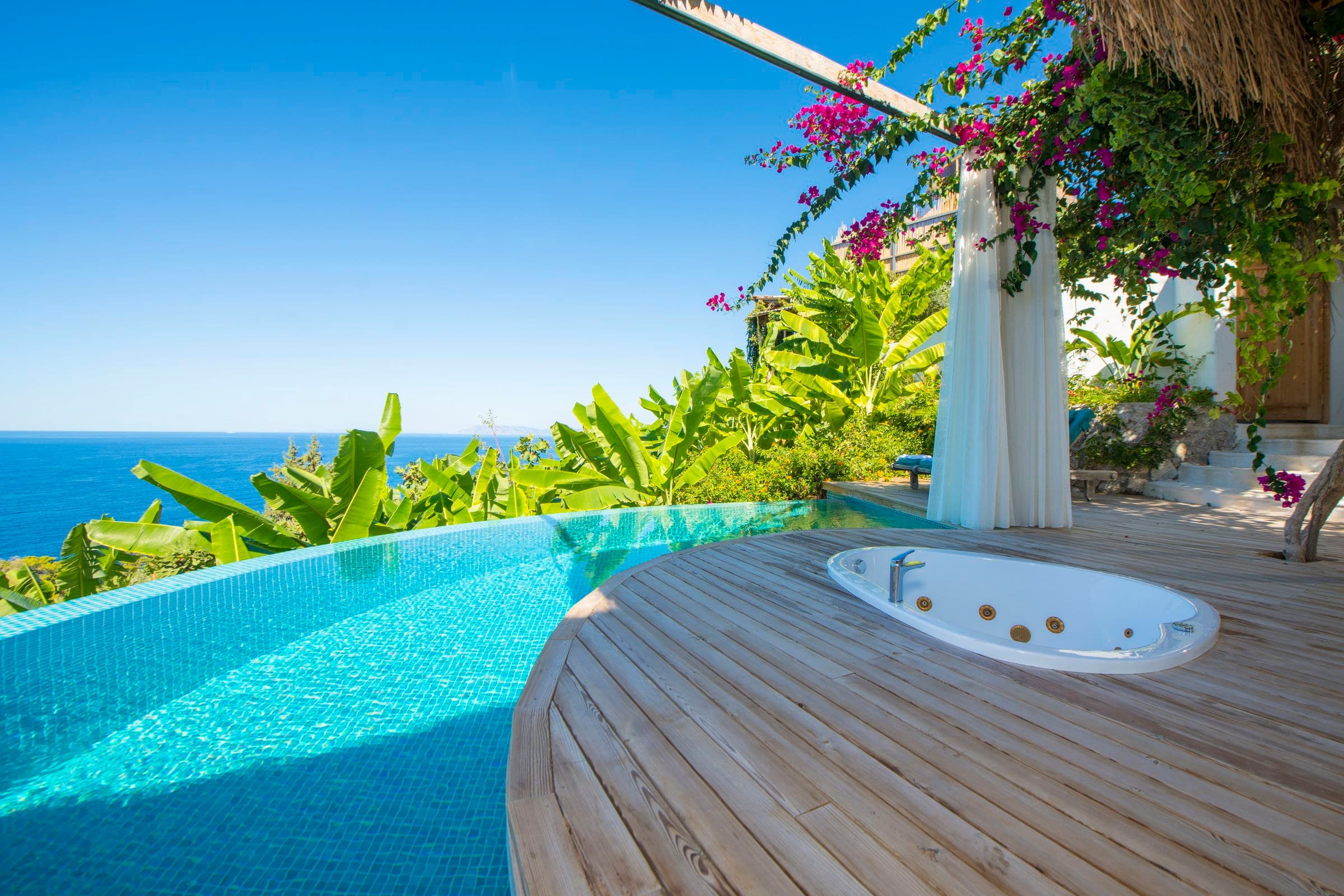 Begonvil: magentafarbene Bougainvillea und Vorhänge, Whirlpool-Insel und geschwungener Infinity-Pool, dahinter das Meer.