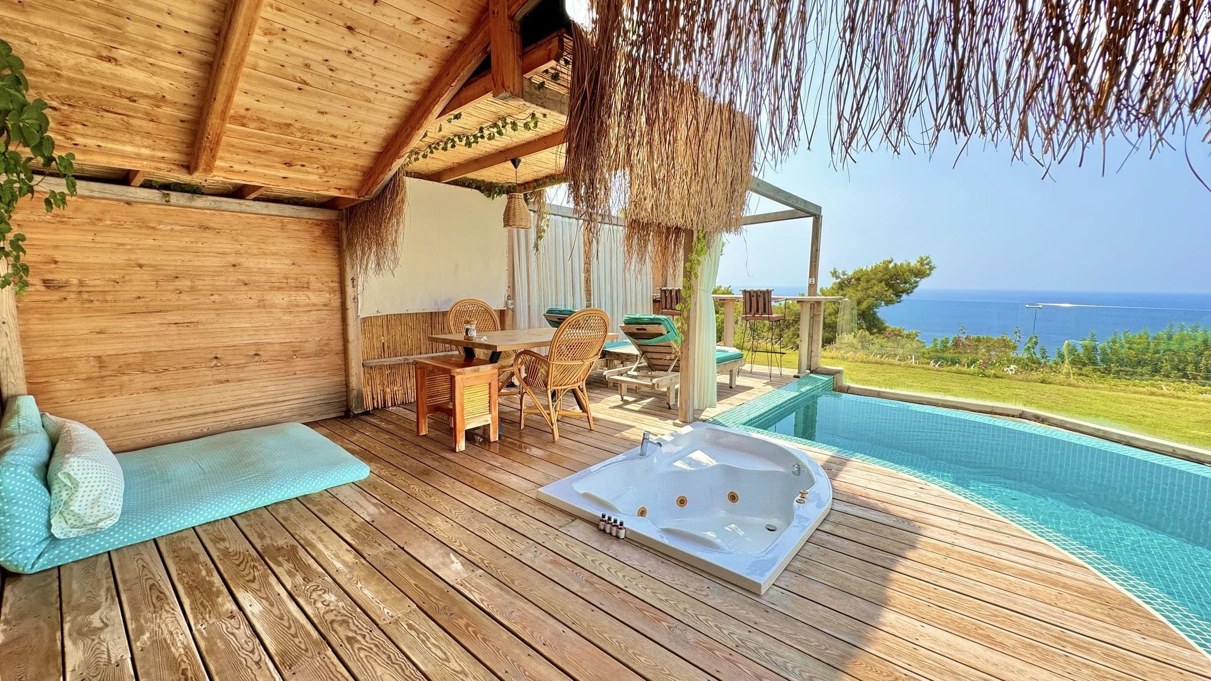Gelincik: Terrasse mit Schilfdach, eingelassener Whirlpool und geschwungener Pool, dahinter das Meer.