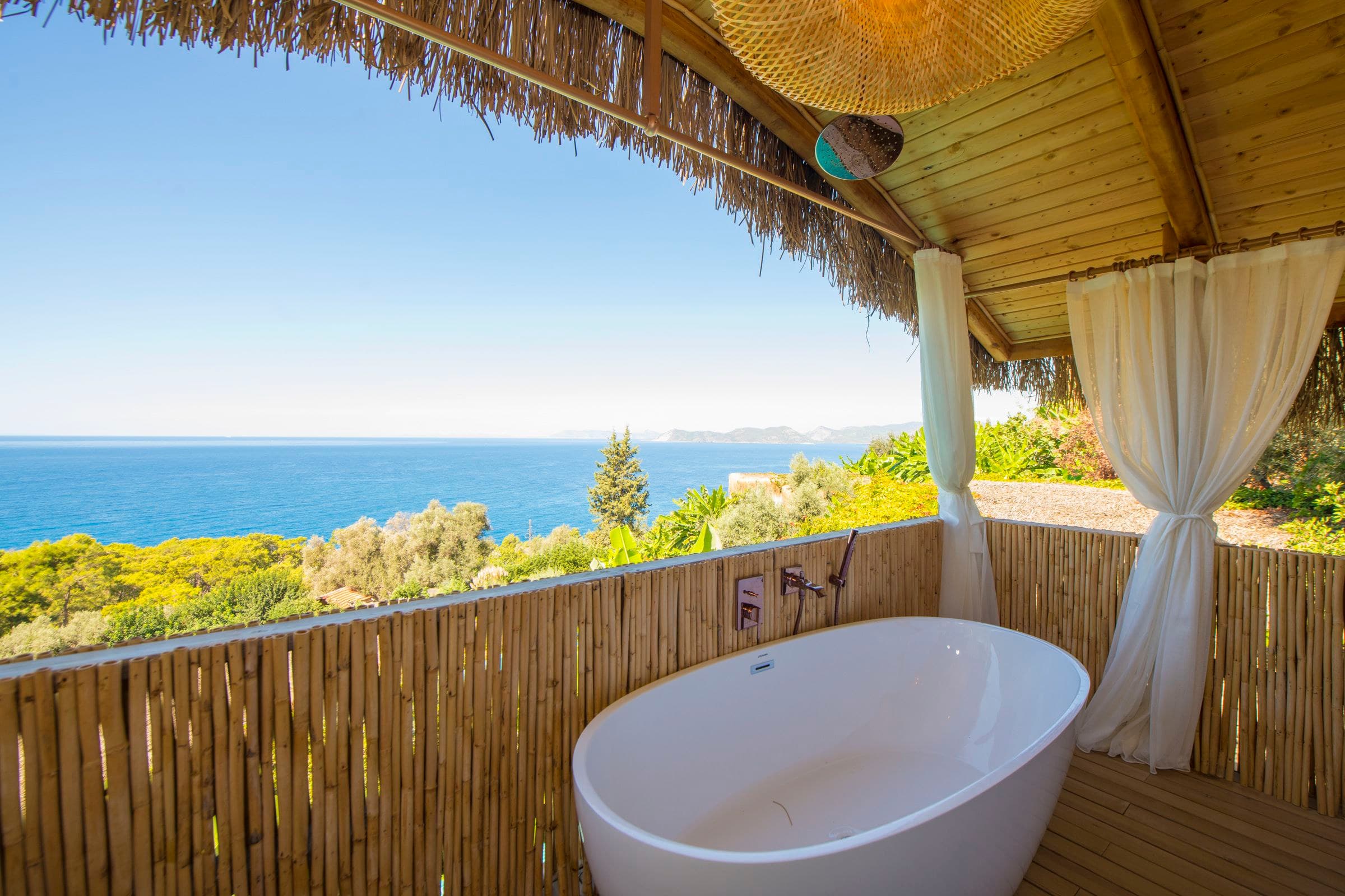 Papatya: freistehende Badewanne auf der oberen Terrasse, Schilfgeländer und Vorhänge, dahinter Meer und Inseln.