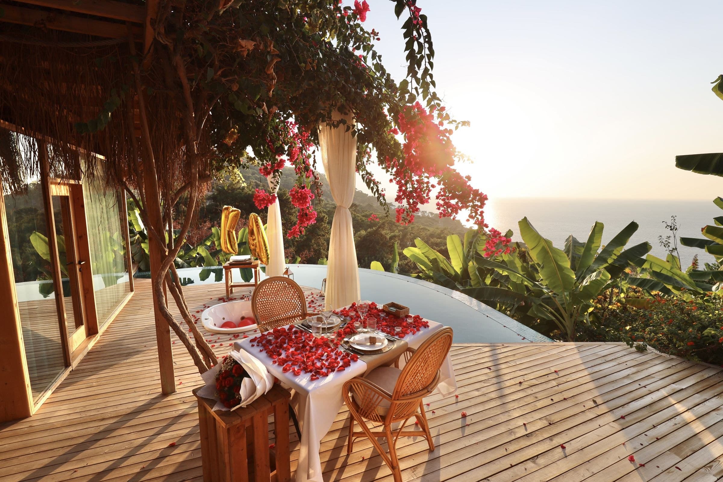 Ein mit Rosenblättern gedeckter Tisch für zwei unter Bougainvillea und Vorhängen, Meer und Sonne.