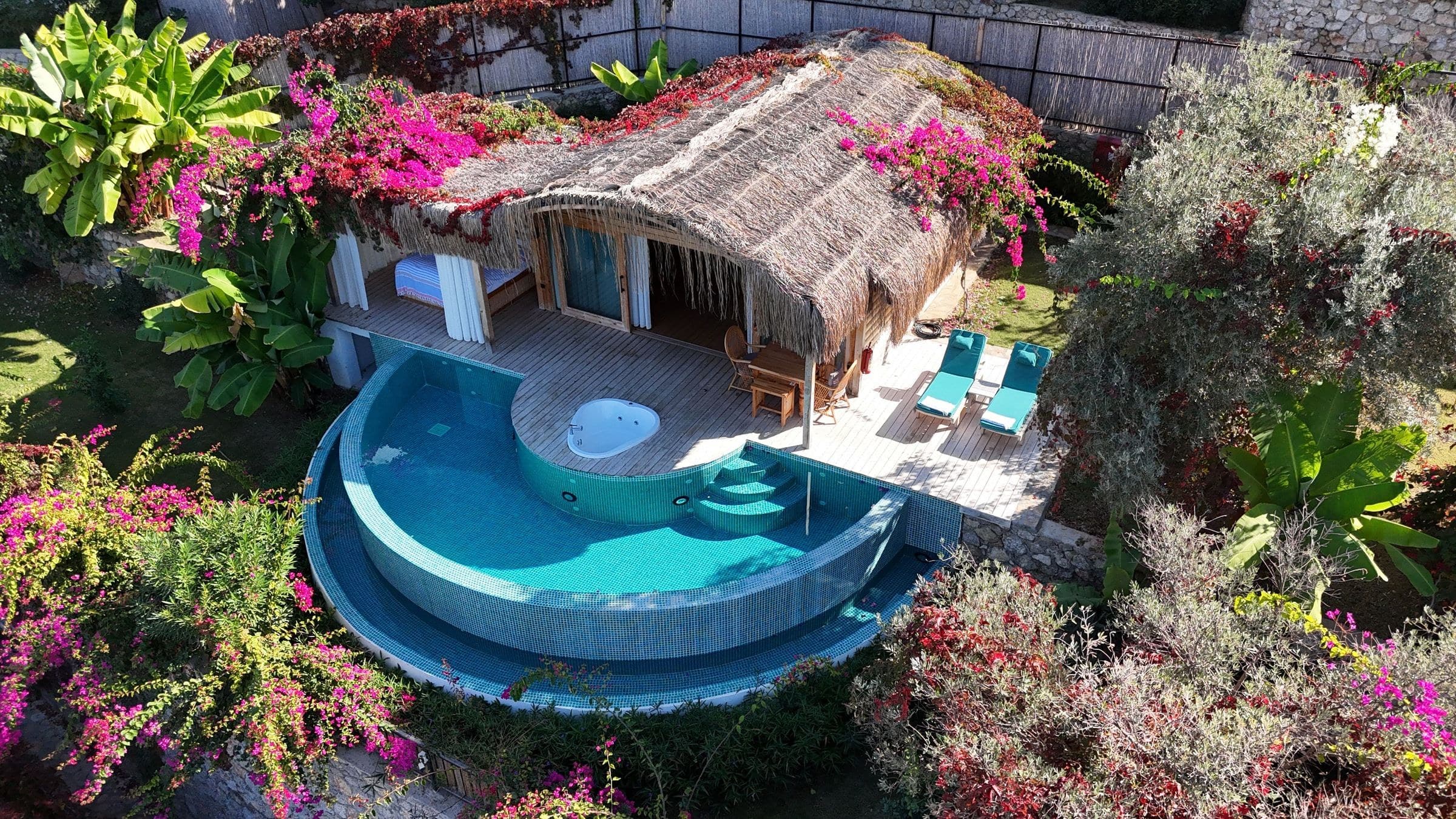 Lotus aus der Drohne: Schilfhütte inmitten magentafarbener Bougainvillea, gestufter halbmondförmiger Pool und herzförmiger Whirlpool.