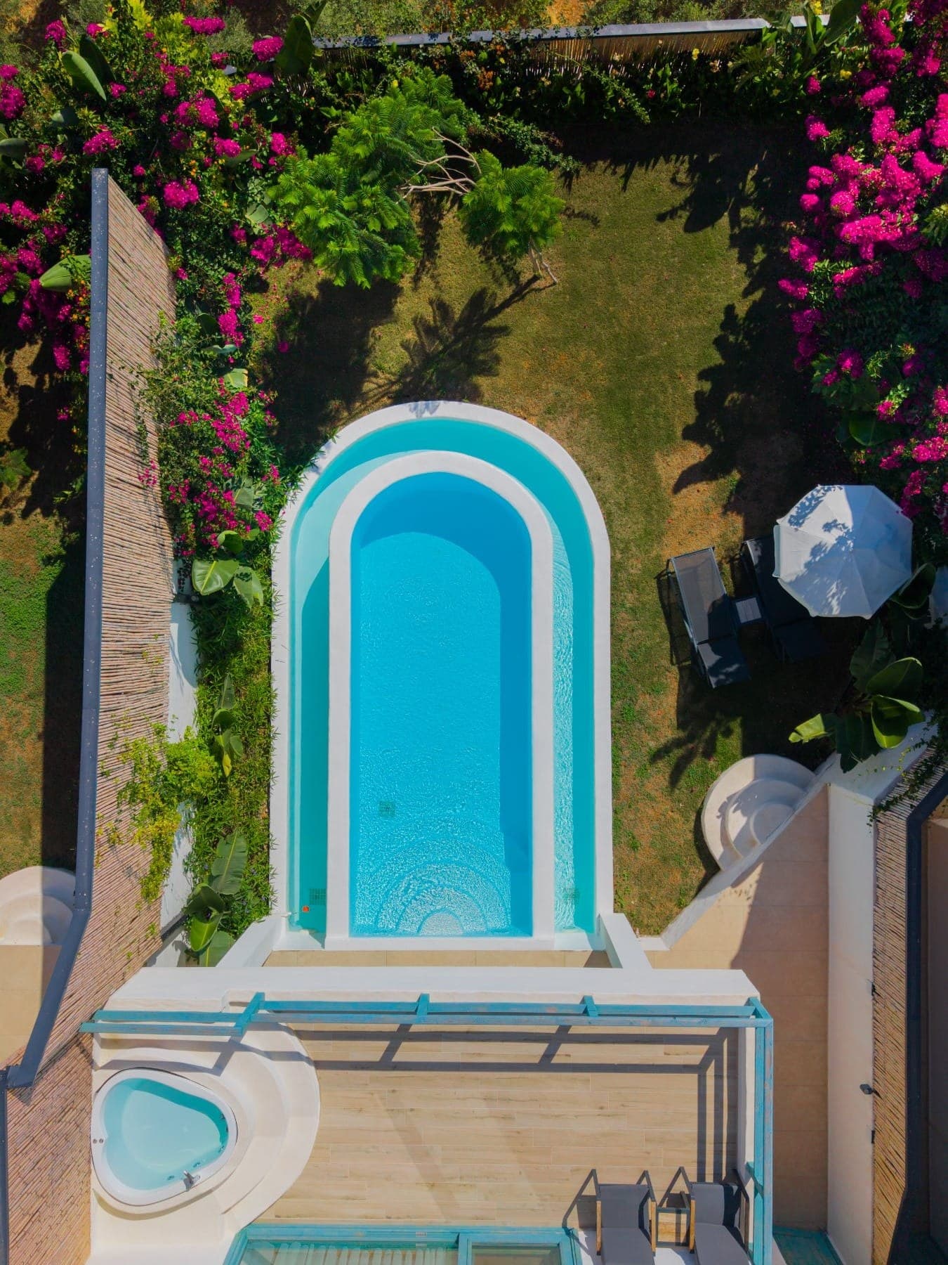 White House von oben: Privatpool mit Bogenabschluss, Bougainvillea, Rasen, Sonnenschirm, Terrassen-Whirlpool und petrolfarbene Pergola.